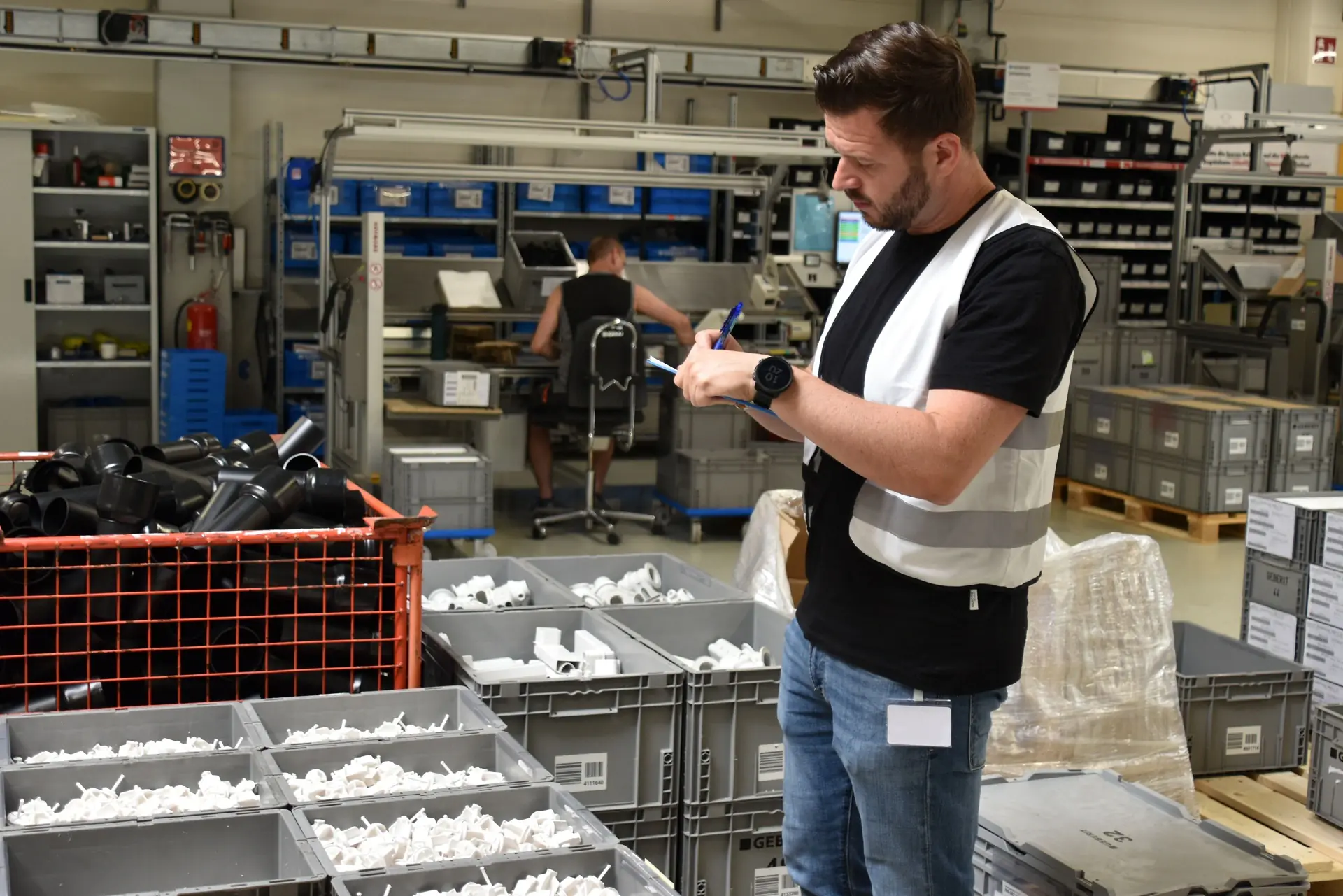 Mitarbeiter führt in einer Produktionshalle eine 5S Überprüfung durch und dokumentiert den Zustand von Materialbehältern und Arbeitsplätzen.